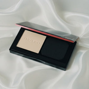 Kompakt puderfoundation i öppet fodral med beige puder, mörk svamp och röd rand