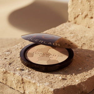 Guerlain bronzerpuder i kompakt ask på sandigt underlag, ljusvarma nyanser