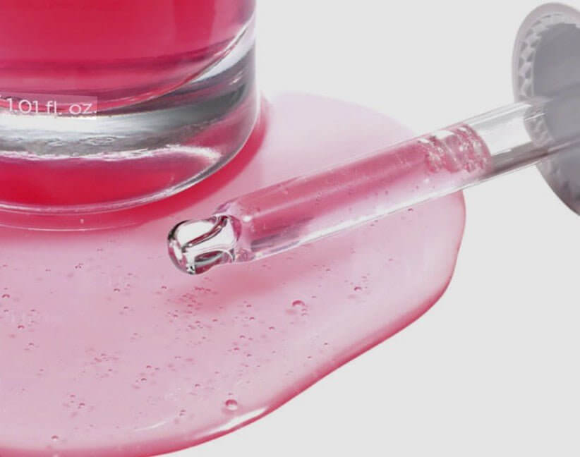 Tranexamsyra TXA serum i en rosa flaska med en pipett på en glansig yta.