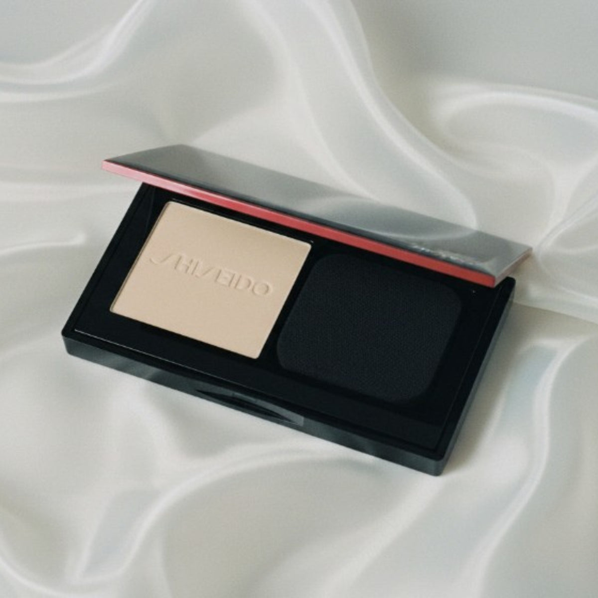 Kompakt puderfoundation i öppet fodral med beige puder, mörk svamp och röd rand