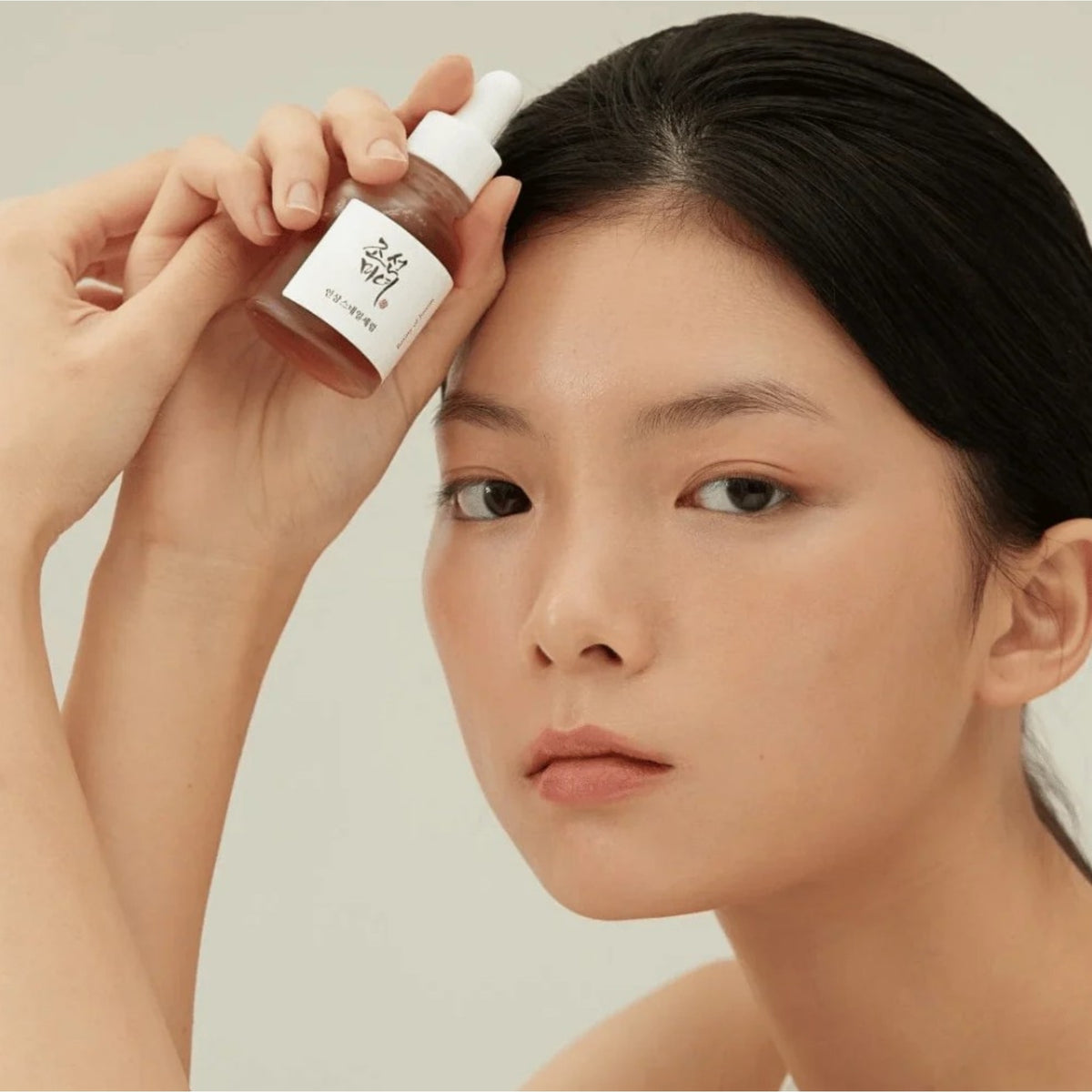 Kvinna som applicerar serum från Beauty of Joseon-flaska vid ansiktet